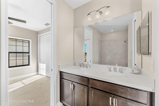 bathroom featuring tiled shower, double vanity, a sink, and visible vents