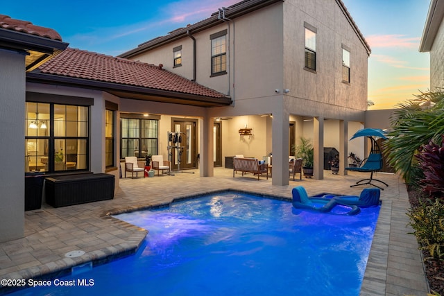 back of house at dusk featuring a patio, an outdoor pool, stucco siding, and a tile roof