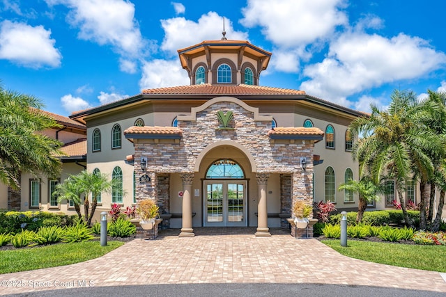 mediterranean / spanish house featuring french doors, stone siding, stucco siding, and a tile roof