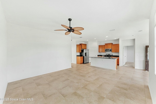 kitchen featuring open floor plan, a ceiling fan, dark countertops, brown cabinets, and stainless steel appliances