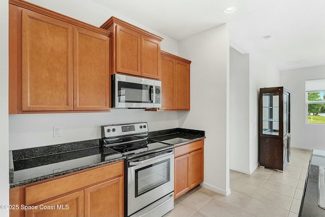kitchen with baseboards, dark stone countertops, light tile patterned floors, brown cabinets, and appliances with stainless steel finishes