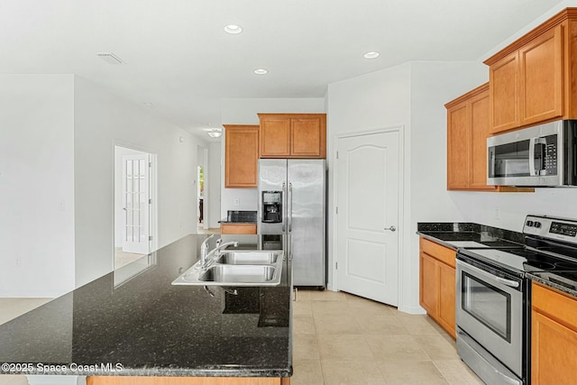 kitchen with brown cabinetry, recessed lighting, appliances with stainless steel finishes, a sink, and a center island with sink
