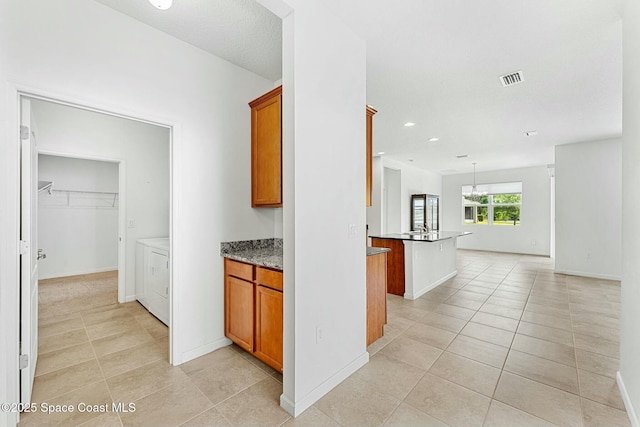 hallway featuring an inviting chandelier, light tile patterned floors, visible vents, baseboards, and washing machine and dryer