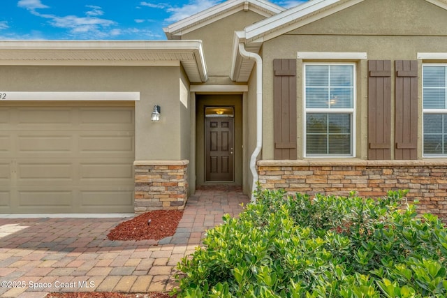 view of exterior entry with a garage, stucco siding, stone siding, and decorative driveway