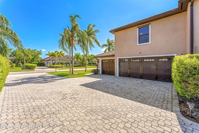 view of property exterior featuring a tile roof, a garage, decorative driveway, and stucco siding