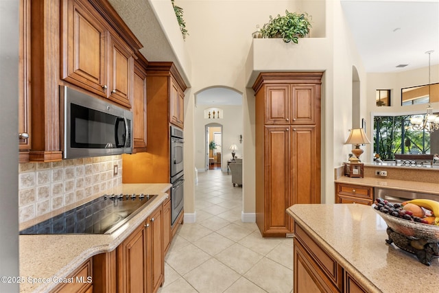 kitchen with arched walkways, brown cabinets, light tile patterned flooring, and appliances with stainless steel finishes