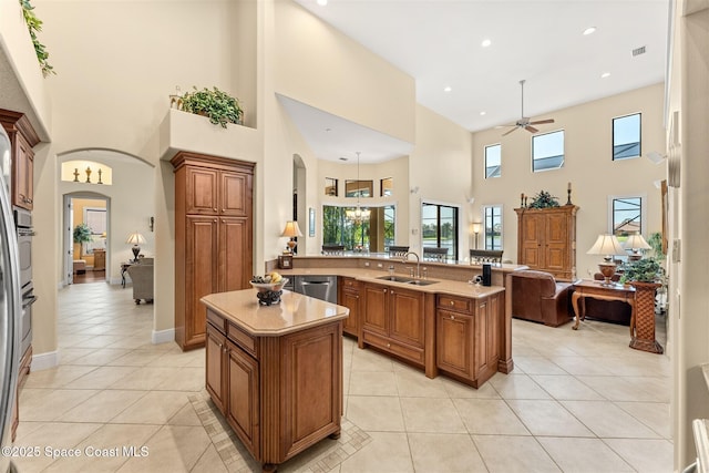 kitchen featuring light tile patterned floors, brown cabinetry, ceiling fan, arched walkways, and a sink