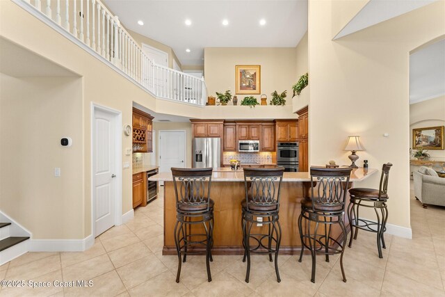 kitchen featuring a towering ceiling, baseboards, a peninsula, brown cabinetry, and stainless steel appliances