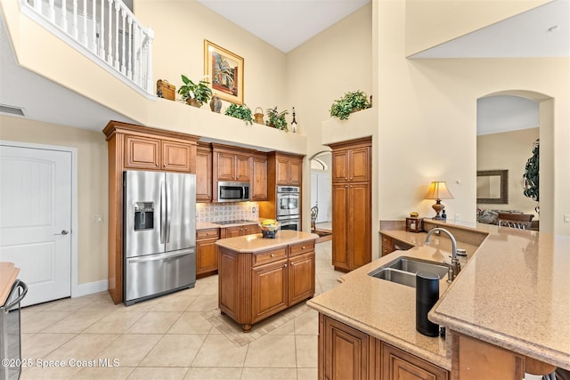 kitchen with brown cabinetry, appliances with stainless steel finishes, a sink, and a towering ceiling