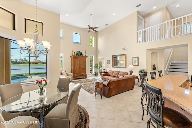 living room with ceiling fan with notable chandelier, light tile patterned floors, visible vents, stairway, and a high ceiling