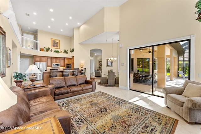 living room with visible vents, arched walkways, a ceiling fan, a towering ceiling, and light tile patterned flooring