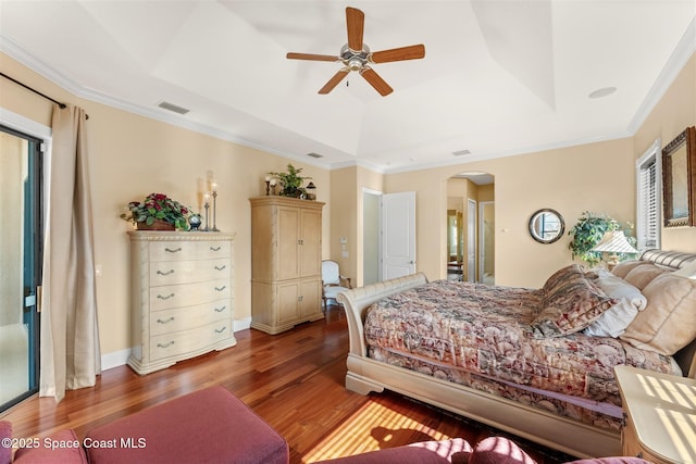 bedroom featuring visible vents, a tray ceiling, multiple windows, arched walkways, and wood finished floors