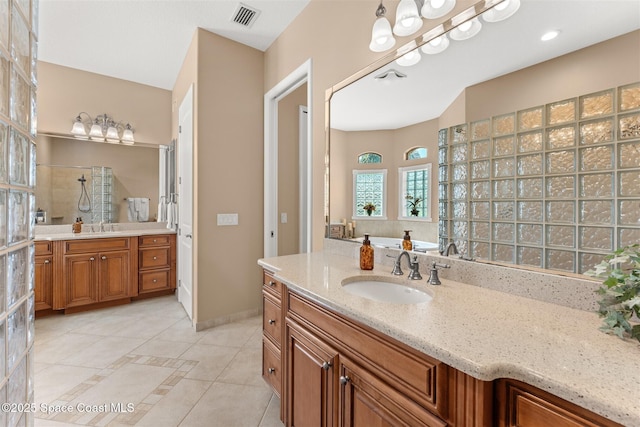 full bath featuring two vanities, tile patterned flooring, tiled shower, visible vents, and a sink