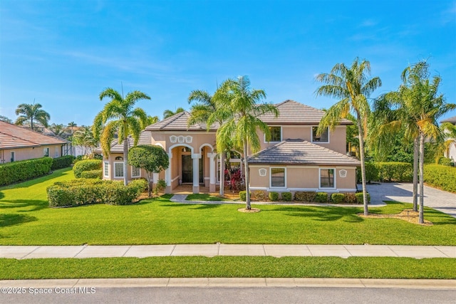 mediterranean / spanish home featuring a tiled roof, stucco siding, and a front yard