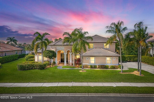 mediterranean / spanish house featuring a tiled roof, driveway, a lawn, and stucco siding