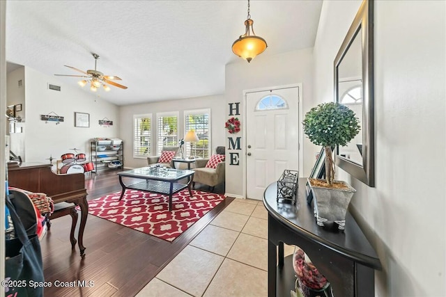 entrance foyer featuring a textured ceiling, a ceiling fan, light tile patterned flooring, visible vents, and lofted ceiling