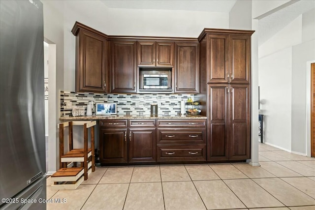 kitchen featuring tasteful backsplash, light tile patterned floors, appliances with stainless steel finishes, dark brown cabinets, and light stone countertops
