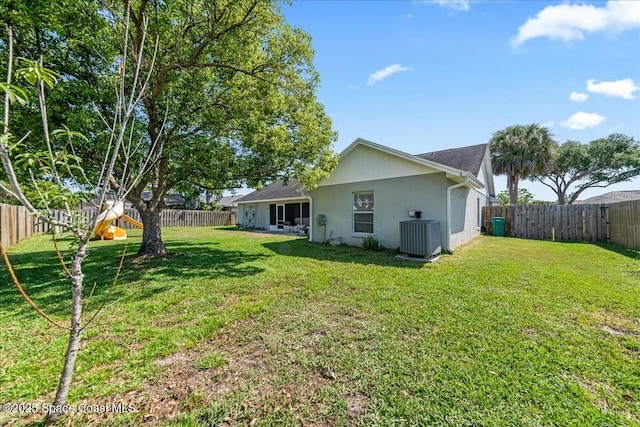 rear view of property featuring central AC unit, a fenced backyard, a lawn, and stucco siding