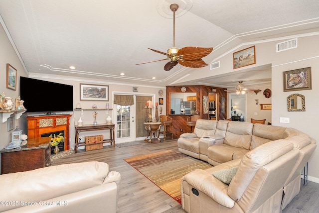 living room with ceiling fan, visible vents, wood finished floors, lofted ceiling, and ornamental molding