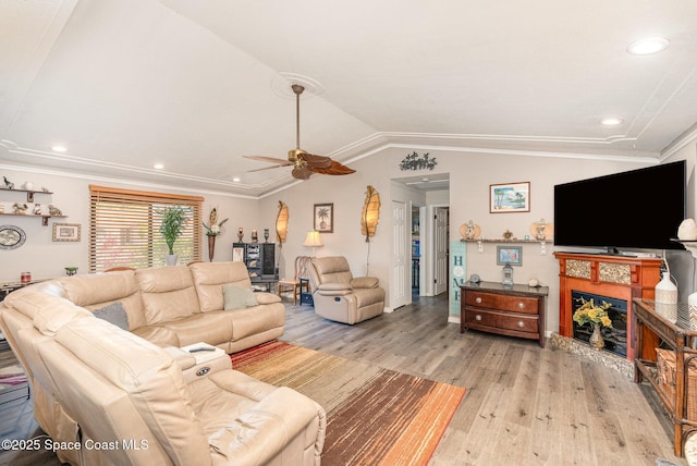 living area with light wood-style floors, vaulted ceiling, a ceiling fan, and a fireplace with raised hearth