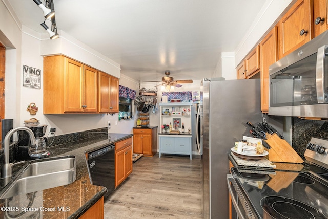 kitchen with a sink, light wood-type flooring, a ceiling fan, dark stone countertops, and appliances with stainless steel finishes