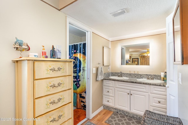 bathroom with double vanity, a sink, a textured ceiling, and wood finished floors