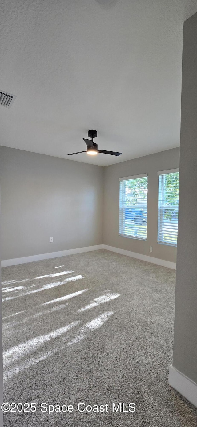 unfurnished room with carpet, visible vents, baseboards, and a ceiling fan