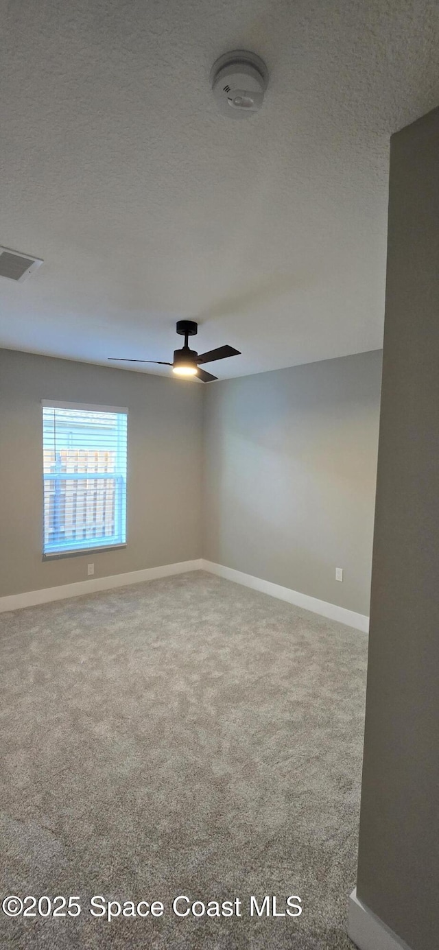 carpeted spare room featuring visible vents, baseboards, a ceiling fan, and a textured ceiling