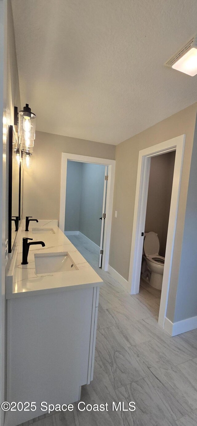 full bath featuring baseboards, double vanity, toilet, marble finish floor, and a sink