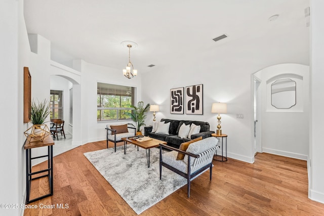 living room featuring light wood finished floors, an inviting chandelier, visible vents, arched walkways, and baseboards