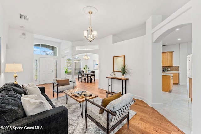 living area with arched walkways, light wood-style flooring, visible vents, and an inviting chandelier