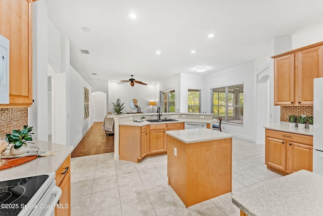 kitchen with tasteful backsplash, a sink, arched walkways, light countertops, and a kitchen island