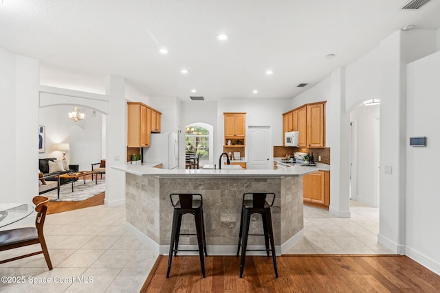 kitchen with arched walkways, a sink, a center island with sink, white appliances, and light countertops