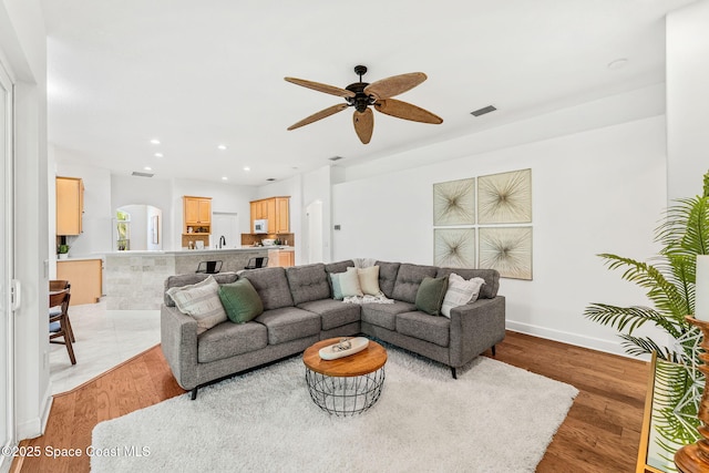 living area featuring arched walkways, light wood-type flooring, visible vents, recessed lighting, and ceiling fan