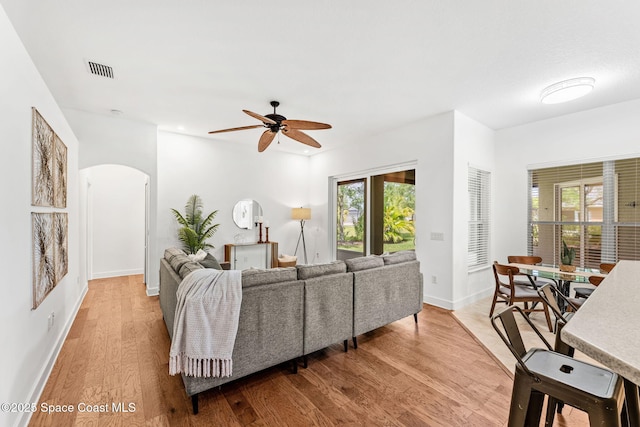 living area featuring ceiling fan, arched walkways, wood finished floors, and a wealth of natural light