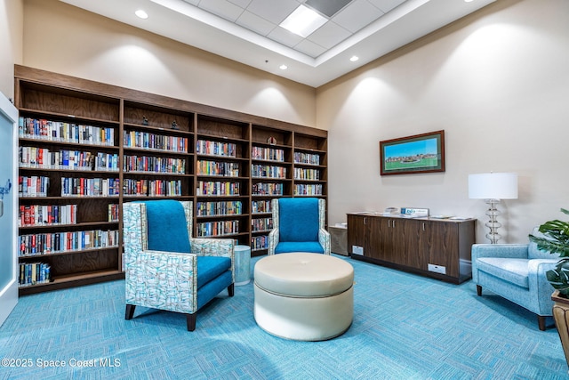 sitting room featuring carpet floors, wall of books, and recessed lighting