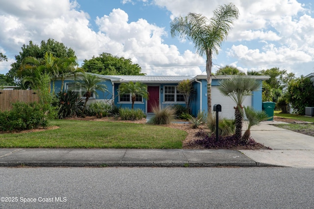 view of front of property with a front yard, fence, metal roof, and driveway