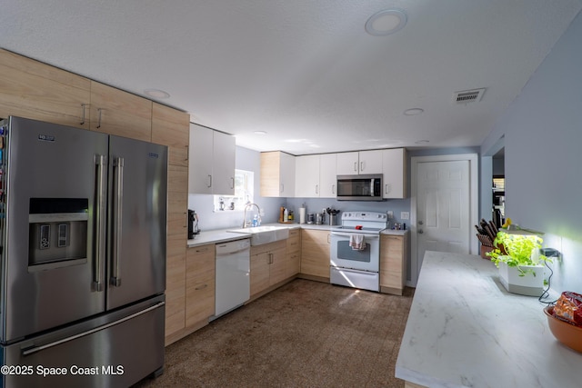 kitchen with light brown cabinets, white cabinets, visible vents, stainless steel appliances, and a sink