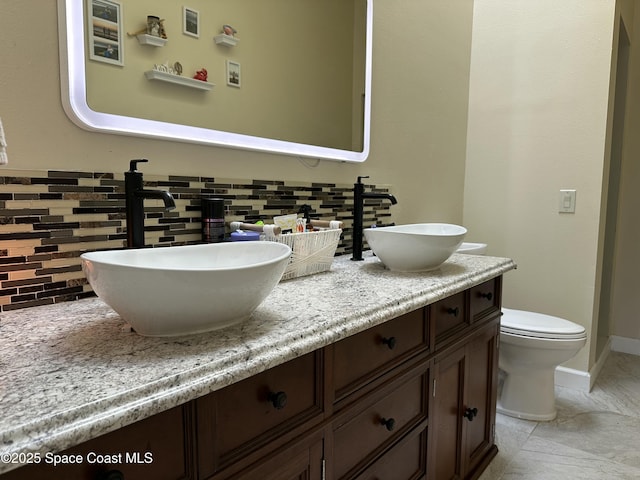 full bathroom featuring a sink, toilet, double vanity, and baseboards