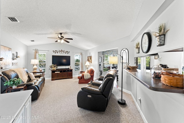 living area with vaulted ceiling, a textured ceiling, a ceiling fan, visible vents, and carpet