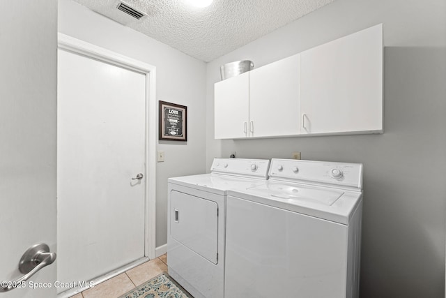 clothes washing area with visible vents, separate washer and dryer, a textured ceiling, cabinet space, and light tile patterned flooring