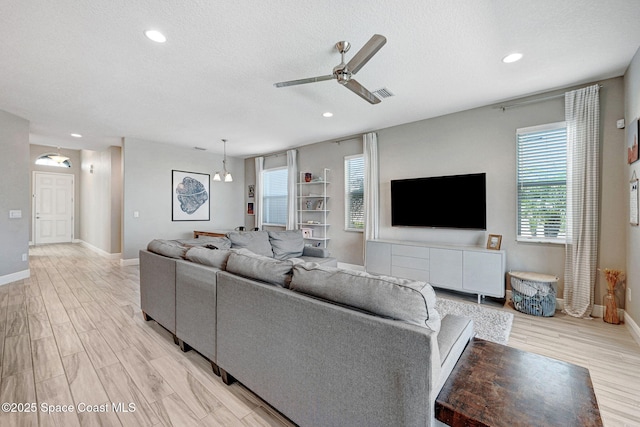 living room featuring light wood-style flooring, a textured ceiling, baseboards, visible vents, and ceiling fan