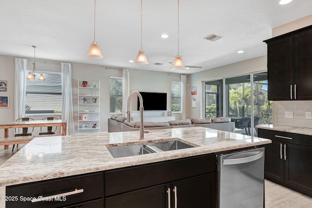 kitchen featuring stainless steel dishwasher, a sink, an island with sink, open floor plan, and light stone countertops