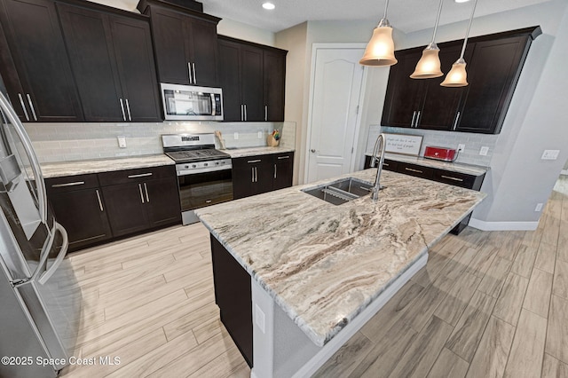 kitchen featuring a sink, light wood-style floors, backsplash, light stone counters, and appliances with stainless steel finishes