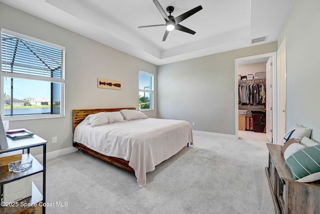 bedroom featuring a tray ceiling, visible vents, a walk in closet, baseboards, and light colored carpet