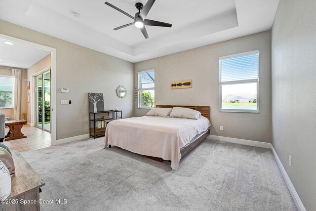 bedroom with a raised ceiling, baseboards, a ceiling fan, and light colored carpet