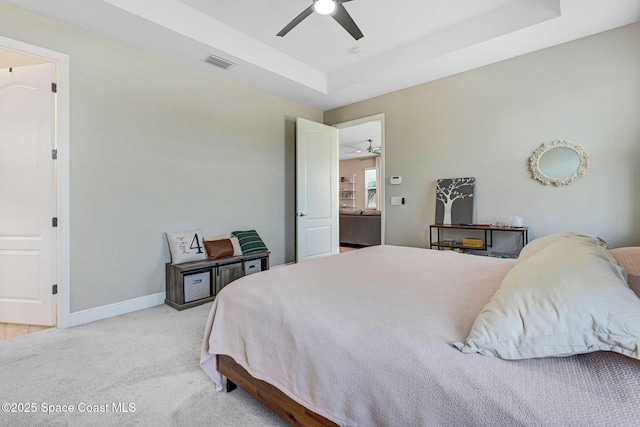 bedroom with light carpet, a tray ceiling, baseboards, visible vents, and a ceiling fan