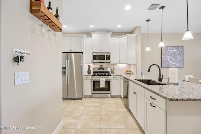 kitchen with a sink, a peninsula, stainless steel appliances, decorative backsplash, and light stone counters