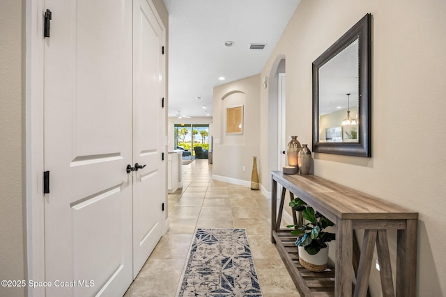 hallway featuring light tile patterned floors, baseboards, recessed lighting, and arched walkways