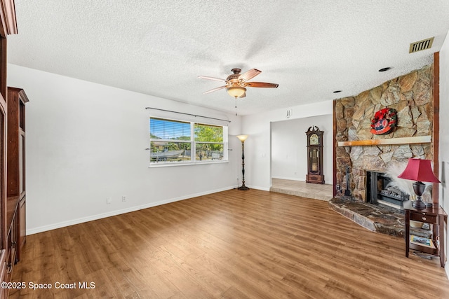 36 Mohican Way, Melbourne Beach, FL 32951 - unfurnished living room with a ceiling fan, light wood finished floors, a textured ceiling, a stone fireplace, and baseboards